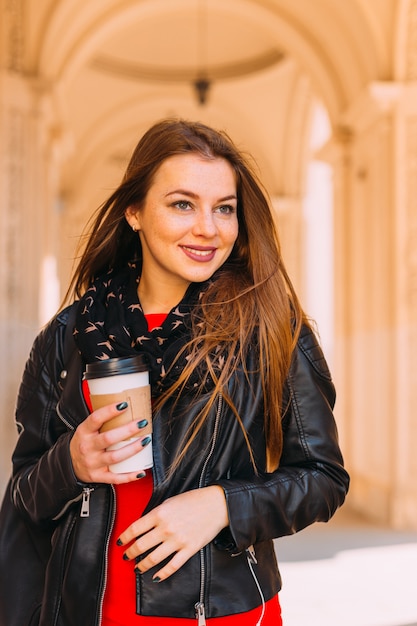 Fille tenant une tasse de café. robe rouge, veste en cuir, sac à dos urbain