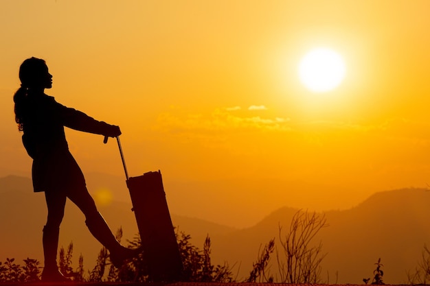 fille tenant une valise au coucher du soleil