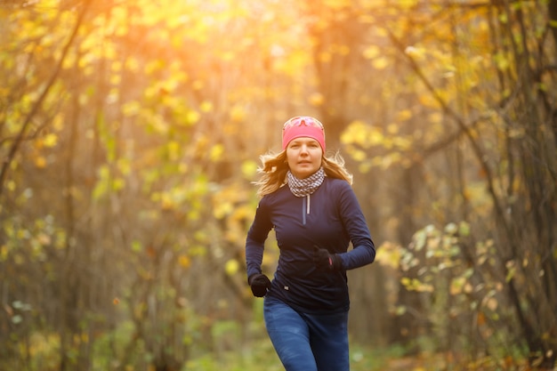 Fille en tenue de sport courant parmi les feuilles d'automne