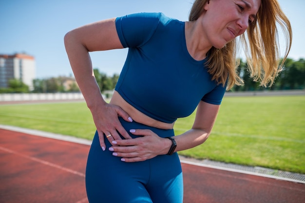 Fille en tenue de sport dans le stade est épuisée et a mal pendant l'entraînement et l'entraînementLa femme sportive a mal au ventre Sports de plein air et concept de douleur