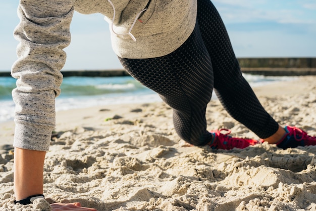 Fille en tenue de sport faisant des exercices sur la plage le matin