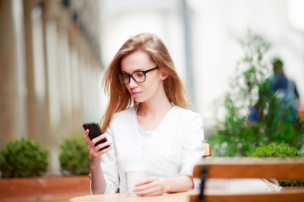 Fille textos sur le téléphone intelligent dans une terrasse de restaurant avec un arrière-plan flou