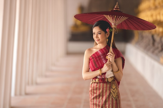 Fille thaïlandaise en costume traditionnel thaïlandais avec un parapluie rouge dans un temple thaïlandais, culture d'identité de la Thaïlande.