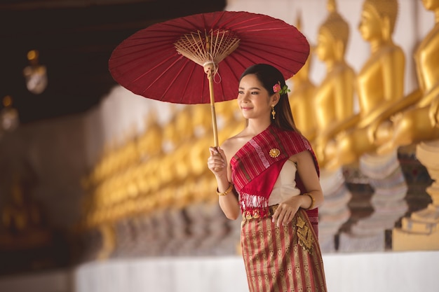 Fille thaïlandaise en costume traditionnel thaïlandais avec un parapluie rouge dans un temple thaïlandais, culture d'identité de la Thaïlande.