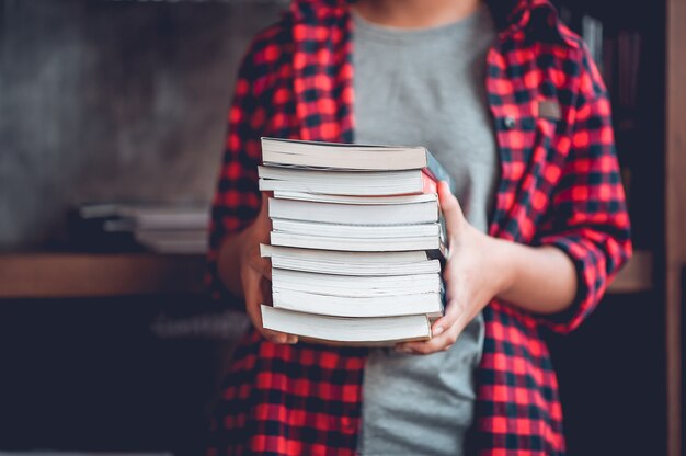 La fille tient beaucoup de livres et dans la bibliothèque.