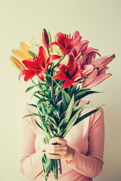 Fille tient un bouquet de lis dans ses mains, cache son visage en fleurs