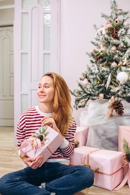 Fille tient un cadeau, arbre de Noël, boîte rose avec un cadeau