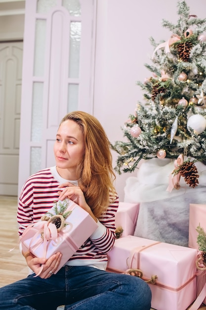 Fille tient un cadeau, arbre de Noël, boîte rose avec un cadeau