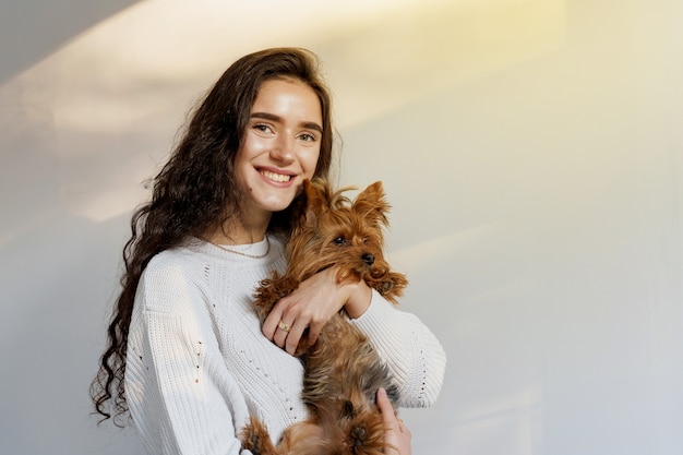 La fille tient le chien brun d'isolement sur le mur blanc