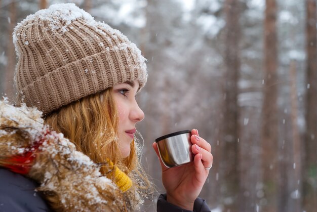 Fille tient dans sa main une tasse de thé (bouchon thermos) à l'extérieur par une journée glaciale