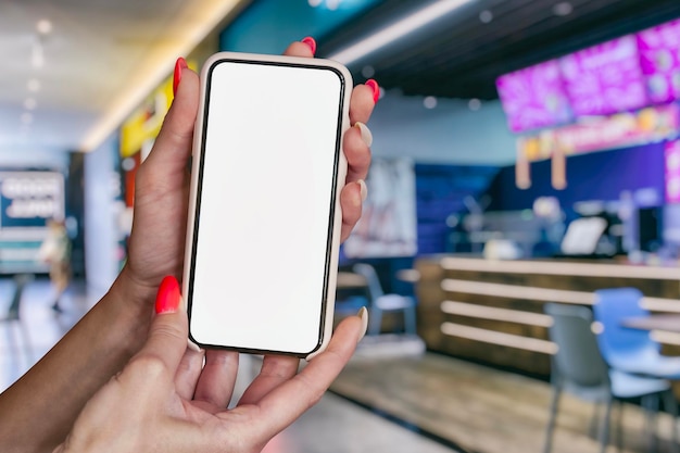 Une fille tient dans ses mains une maquette d'un smartphone avec un écran blanc sur fond de l'aire de restauration