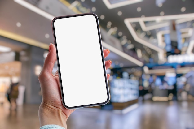 Photo une fille tient dans ses mains une maquette d'un smartphone avec un écran blanc sur fond de supermarché