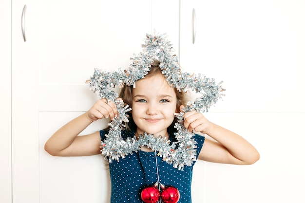 Une fille tient une étoile dans ses mains pour décorer la maison pour le nouvel an et Noël, l'enfant se prépare pour les vacances, aide les parents, attend des cadeaux