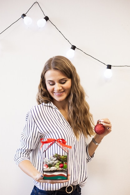 Une fille tient un florariumov, en forme de verre avec des plantes succulentes, des pierres et du sable, décoré de rubans de Noël. Cadeaux de Noël pour la maison et le bureau