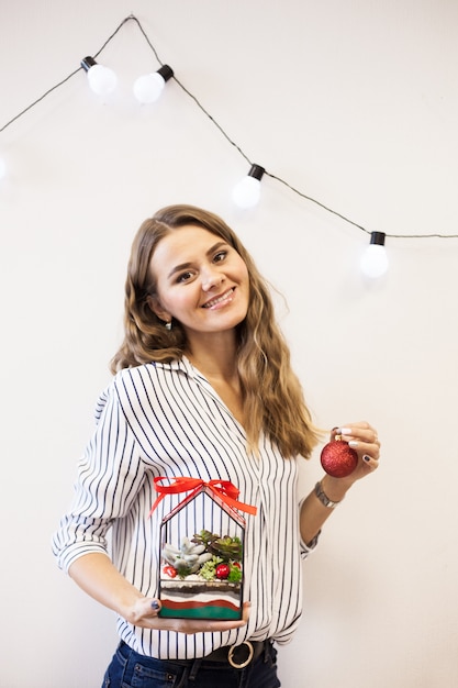 Une fille tient un florariumov, forme de verre avec des plantes succulentes, des pierres et du sable, décoré avec des rubans de Noël. Cadeaux de Noël pour la maison et le bureau.