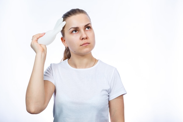 La fille tient des gants médicaux blancs dans ses mains. Protection contre les germes et le virus. Elle est en T-shirt blanc sur fond blanc.