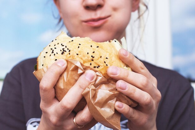 La fille tient un gros hamburger. Arrière-plan flou doux. mode de vie