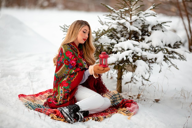 Une fille tient une lampe de poche dans ses mains dans la neige en hiver foulard rouge folk ukrainien