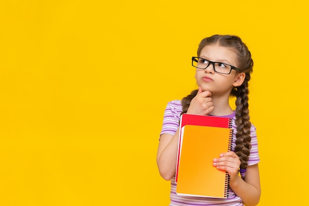 La fille tient un livre et regarde au loin Jolie petite fille sur fond jaune isolé