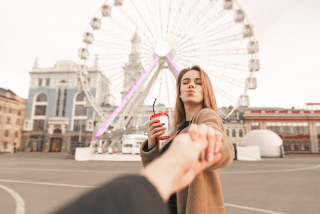 Fille tient la main de son petit ami et fait un baiser aérien dans le contexte du paysage de la ville. L'amour. Suivez-moi