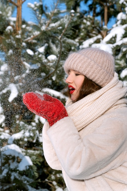 La fille tient la neige et souffle dessus. Portrait de jeune femme au chapeau d'hiver.