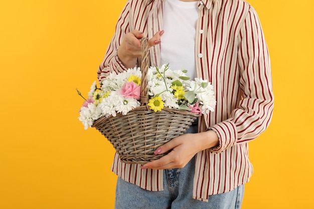 La fille tient le panier des fleurs sur le fond jaune