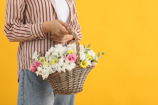 La fille tient le panier des fleurs sur le fond jaune