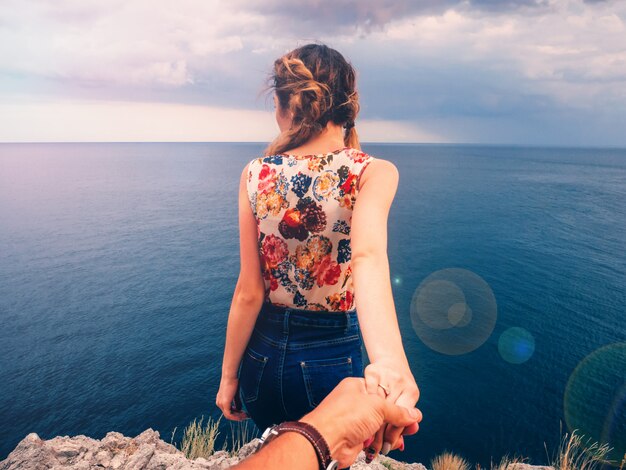 Fille tient son petit ami la main contre la mer sur une falaise un jour d'été