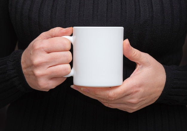 Fille tient une tasse blanche dans les mains.