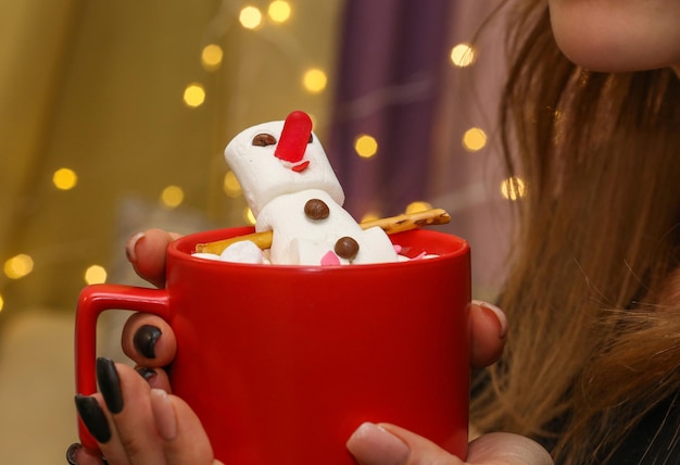 une fille tient une tasse rouge avec un bonhomme de neige guimauve dans ses mains