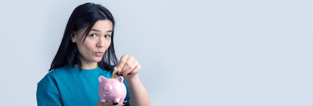 La fille tient une tirelire rose et une pièce dans ses mains. Le concept de richesse et d'accumulation.