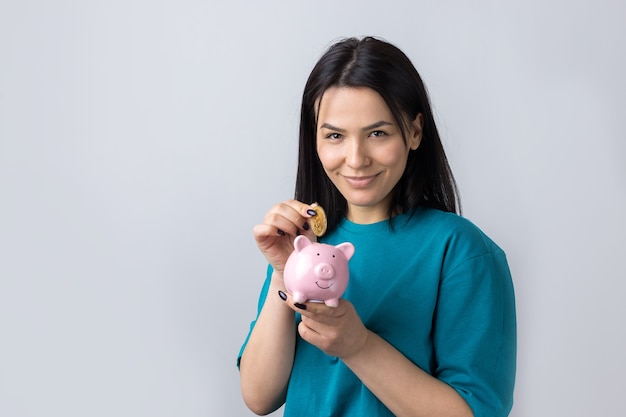 La fille tient une tirelire rose et une pièce de monnaie dans ses mains. Le concept de richesse et d'accumulation.