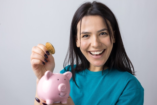 La fille tient une tirelire rose et une pièce de monnaie dans ses mains. Le concept de richesse et d'accumulation.