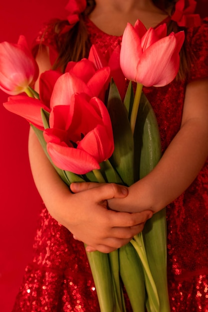 Une fille tient des tulipes rouges sur fond rouge sans visage Photo de haute qualité