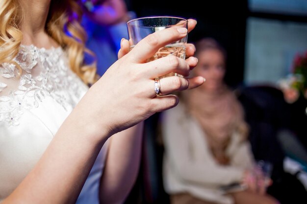 La fille tient un verre d'alcool. Belle mariée avec un maquillage élégant en robe blanche.