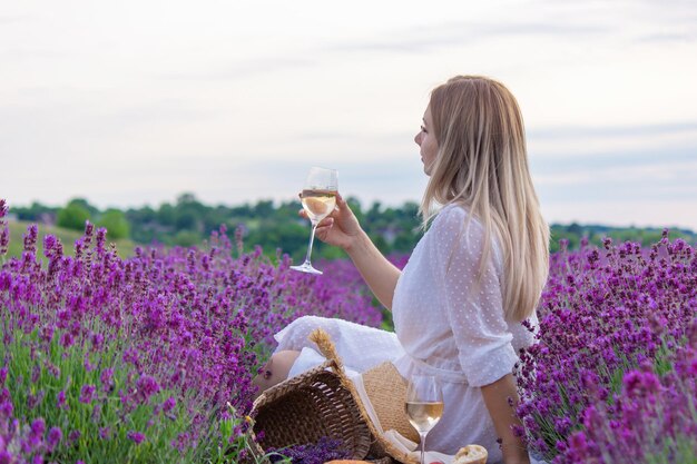 Une fille tient un verre de vin blanc sur fond de champ de lavande Une fille boit du vin dans un champ de lavande