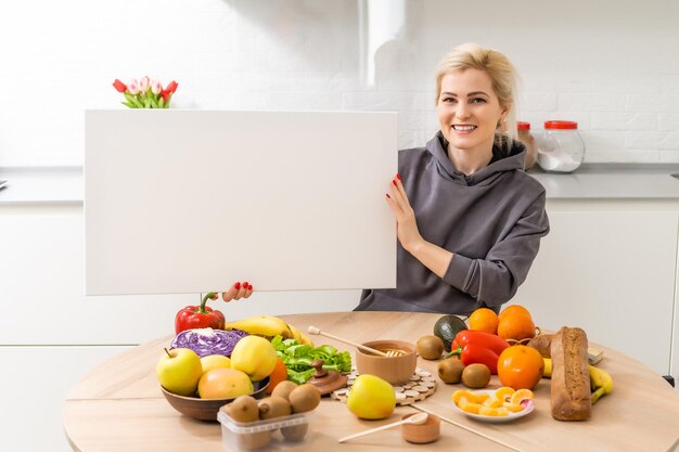 Fille et toile vierge. Copiez l'espace sur le tableau de toile pour l'image ou le message. Jeune femme regardant une maquette d'affiche sur la cuisine près des légumes.