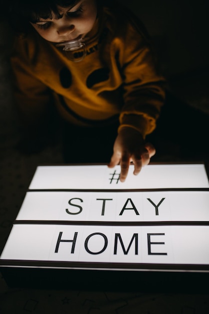 Photo fille touchant boîte lumineuse avec texte rester à la maison dans la chambre noire