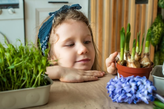 Fille transplante des fleurs et des plantes d'intérieur un enfant dans un bandana plantes bulbes jacinthes microgreens