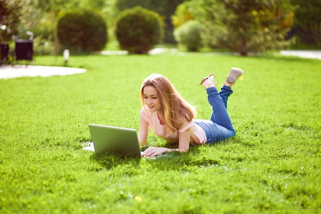 Fille travaillant dans un ordinateur portable allongé sur l'herbe dans le parc