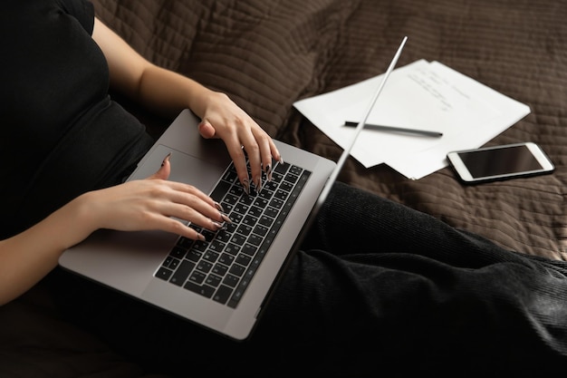 Fille travaillant à la maison à l'ordinateur allongé sur le lit