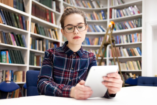 Fille travaillant avec tablette assis dans la bibliothèque.