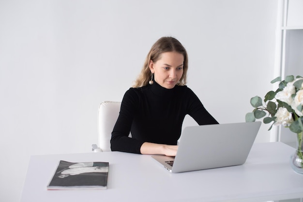 Une fille travaille dans un bureau blanc avec un ordinateur portable