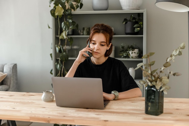 La fille travaille à l'ordinateur et parle au téléphone