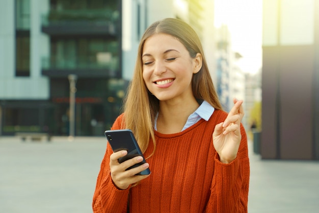 Fille traversant les doigts et mord la lèvre tenant le téléphone en attente de bonnes nouvelles