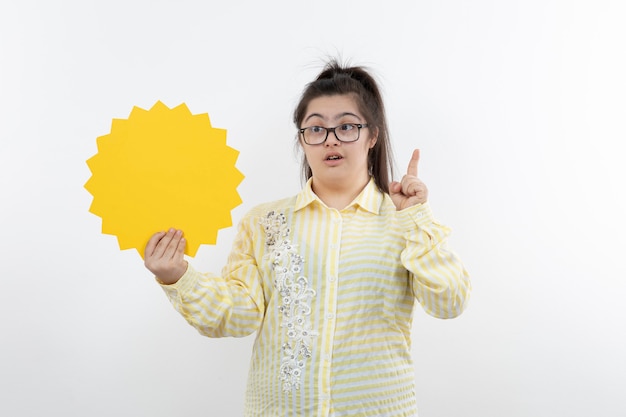 Fille trisomique à lunettes debout avec bulle de dialogue vide.