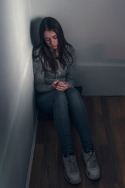 Fille triste assis sur le sol dans le coin de la chambre