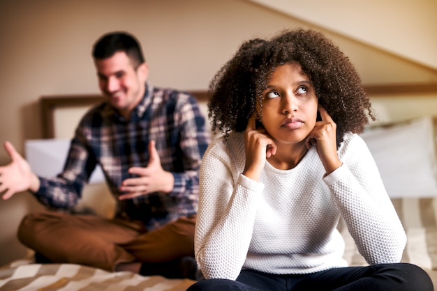 Une fille triste est assise devant son petit ami avec les doigts dans les oreilles.