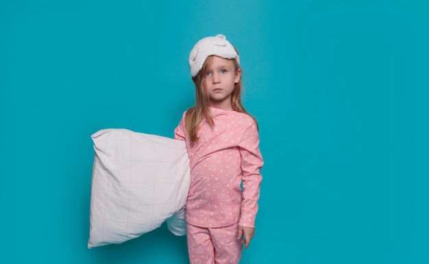 Une fille triste en pyjama et avec un oreiller dans les mains se dresse sur un fond bleu