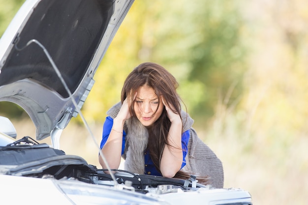 Fille triste avec une voiture cassée avec capot ouvert